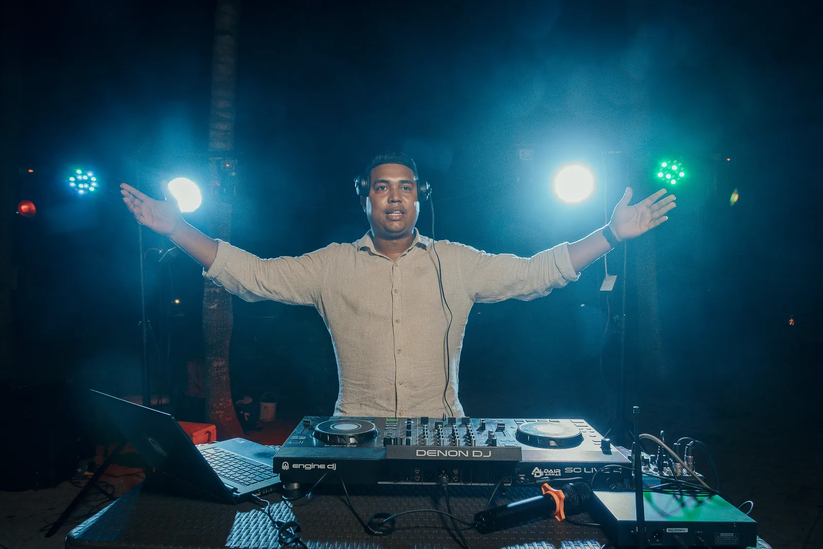 DJ performing behind the decks under stage lighting at an evening event